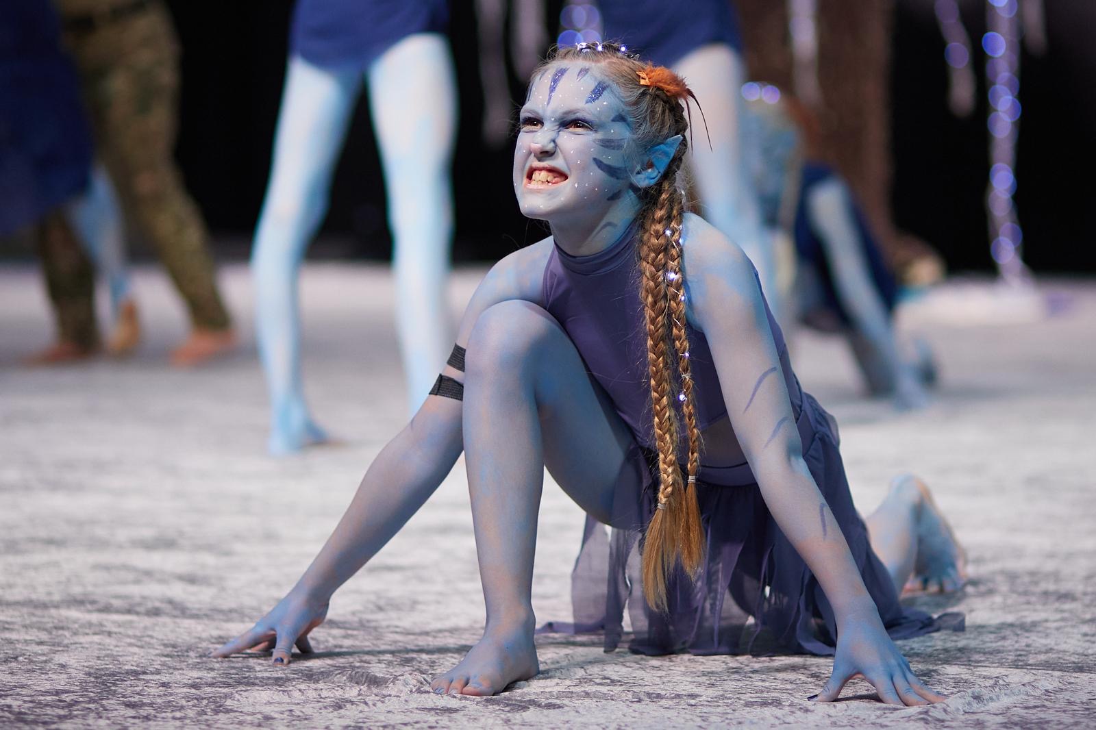 Verkleidetes junges Mitglied von Confianza in blauer Ganzkörperbemalung und Fantasy-Kostüm, in ausdrucksstarker Pose auf dem Boden kniend.